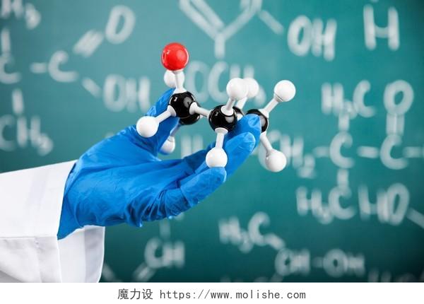 在黑板前一位学者手中拿着一个分子结构模型